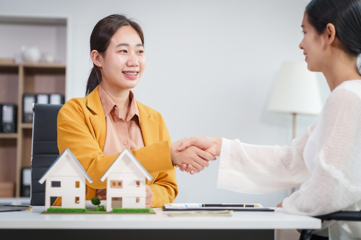 Asian businesswoman discusses home purchase contracts with clients at her desk, focusing on loans